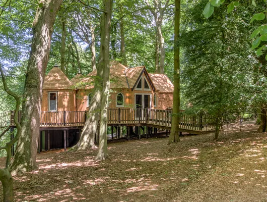 Treehouse with a turret and gabled porch on a raised deck across the wooded hillside at Cedar Hollow Oxford